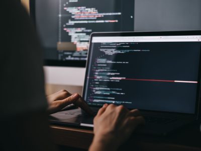 Young caucasian female programmer in glasses writes program code on a laptop computer. home office