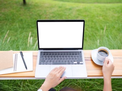 Top view mockup image of a woman using laptop computer with blank white desktop screen while working in the outdoors